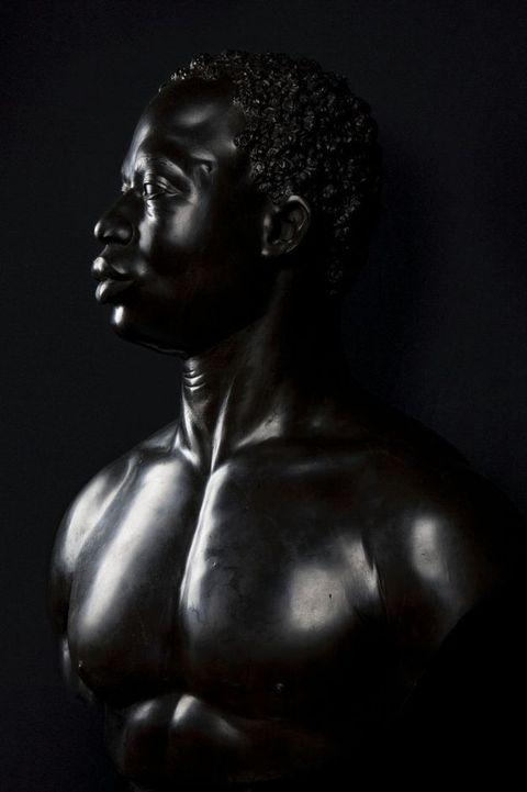 Photograph. Edges of a sculpture disappear against a deep black background. The sculpture faces our left in profile and nearly fills the picture.